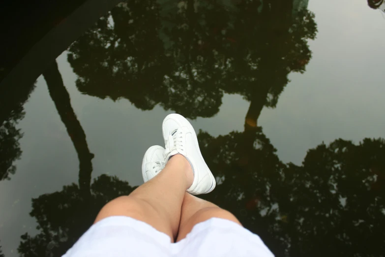 a person standing in front of a pond with trees reflected in the water, a picture, aestheticism, wearing white sneakers, lying down, white hue, view from below