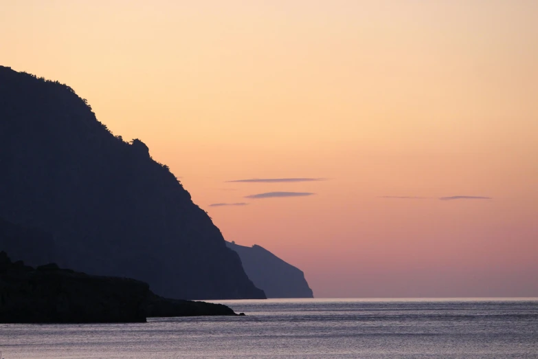 a large body of water with a mountain in the background, by Exekias, pexels contest winner, romanticism, cliff side at dusk, john pawson, cinq terre, at gentle dawn pink light