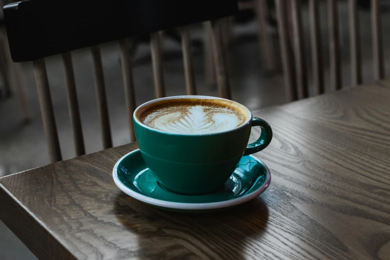 a cup of coffee sitting on top of a wooden table, inspired by Elsa Bleda, pexels contest winner, renaissance, dark green color scheme, cappuccino, three - quarter view, uk