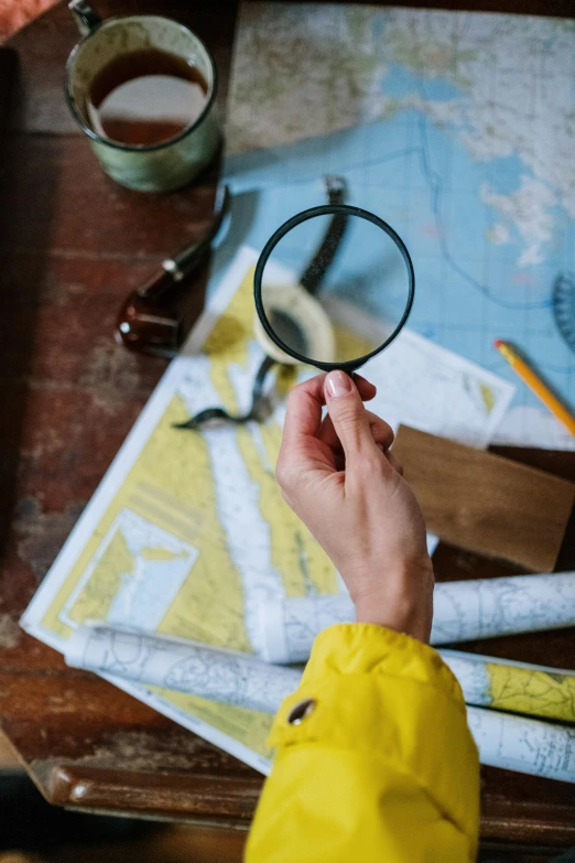 a person looking through a magnifying glass, visual art, nautical maps, yellow, tabletop, adventure gear