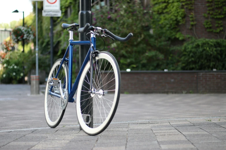 a blue bicycle is chained to a pole, by Niels Lergaard, unsplash, with big chrome tubes, porcelain skin ”, midnight blue, dezeen