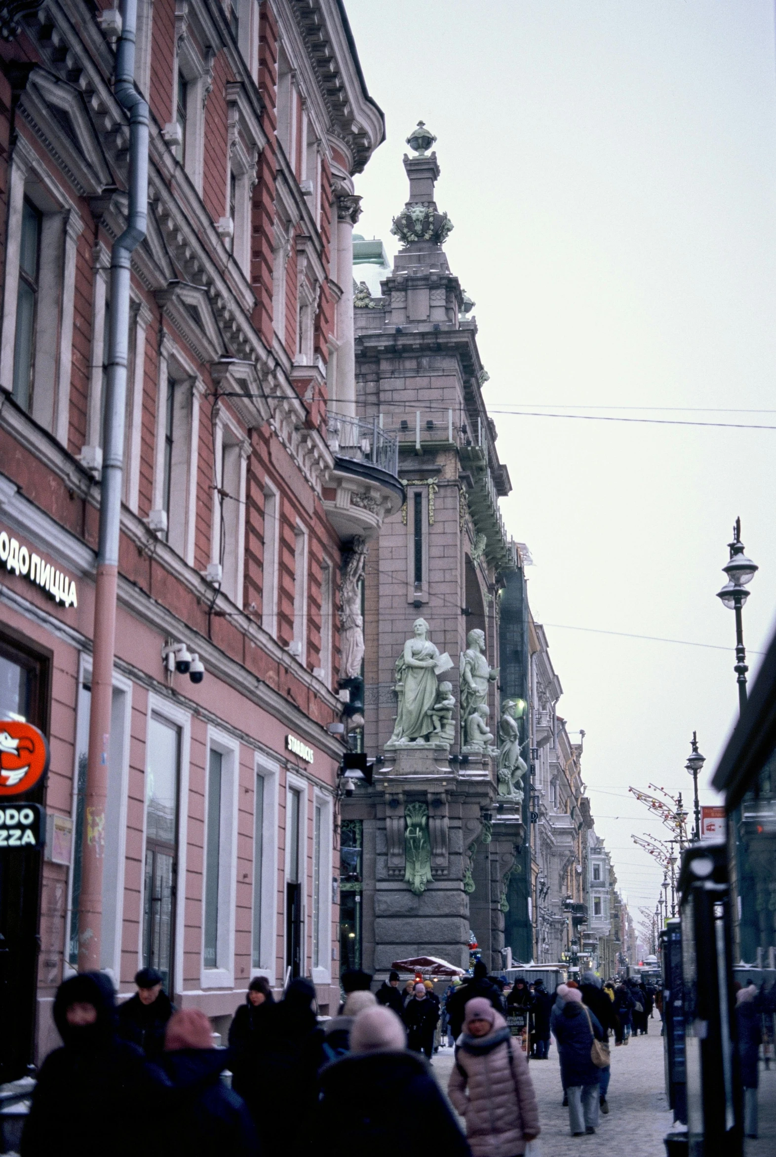 a group of people walking down a street next to tall buildings, a statue, art nouveau, denmark, rococo architecture, drugstore, a 35mm photo