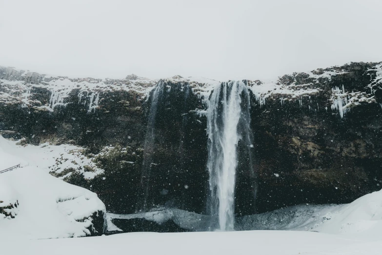 a person standing in front of a waterfall in the snow, pexels contest winner, hurufiyya, seen from afar, waterfall falling down, grey, snowy plains