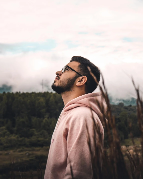 a man in a pink hoodie looking up at the sky, trending on pexels, jewish young man with glasses, lush vista, lgbt, wearing a grey robe