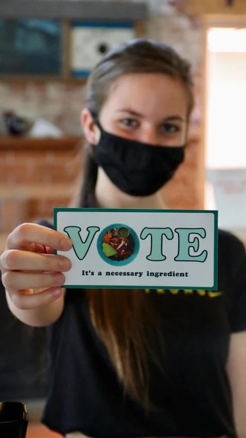 a woman wearing a face mask holding up a vote sign, by Carey Morris, cg society contest winner, renaissance, edible, sticker design, a green, a horned