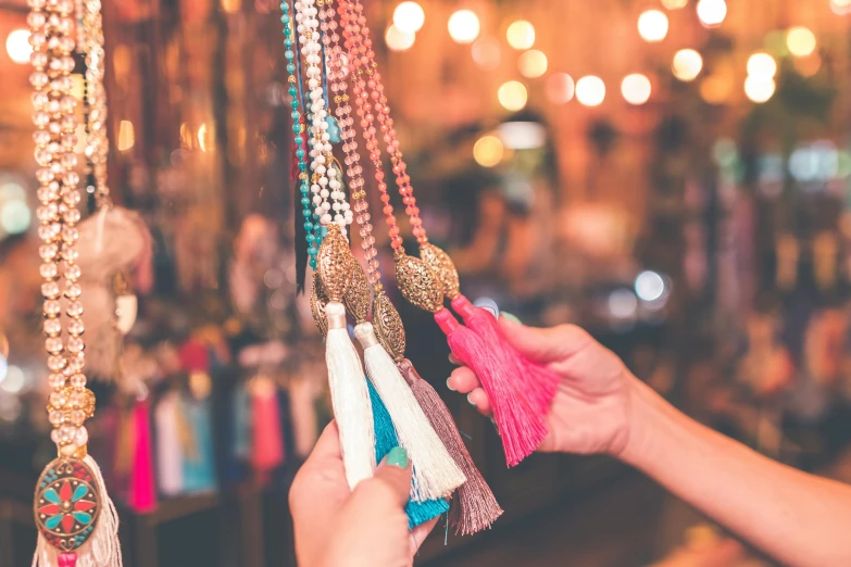 a woman holding a bunch of tassels in her hand, a photo, trending on pexels, arts and crafts movement, neon shops, necklace on display, retro stylised, pink and blue colour