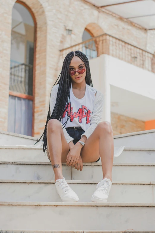 a woman sitting on the steps of a building, by Afewerk Tekle, pexels contest winner, graffiti, wavy long black hair and glasses, white t-shirt with red sleeves, white black fade braided hair, full body cute young lady