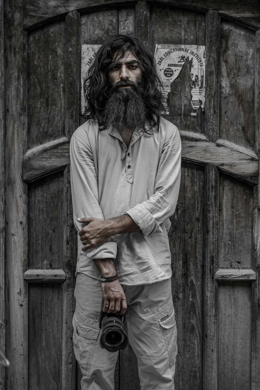 a man standing in front of a wooden door, an album cover, pexels contest winner, very long white beard and hair, dressed in a ((ragged)), vastayan, grey clothes