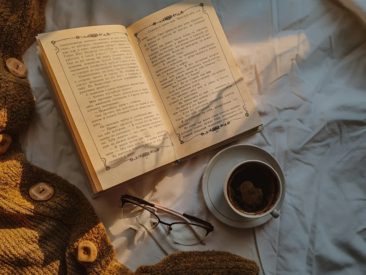 an open book sitting on top of a bed next to a cup of coffee, a cross stitch, pexels contest winner, romanticism, brown clothes, wearing small round glasses, thumbnail, high angle shot