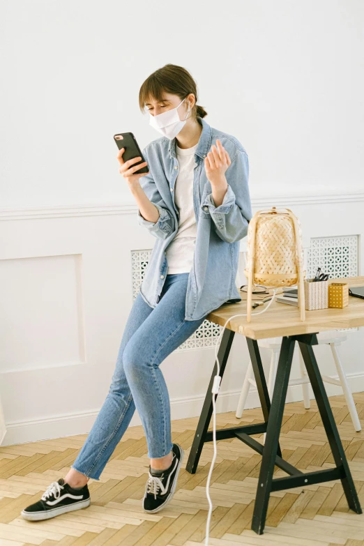 a woman sitting on a chair using a cell phone, a picture, by Miyamoto, trending on pexels, happening, plague and fever. full body, wearing denim, dust mask, pastel'