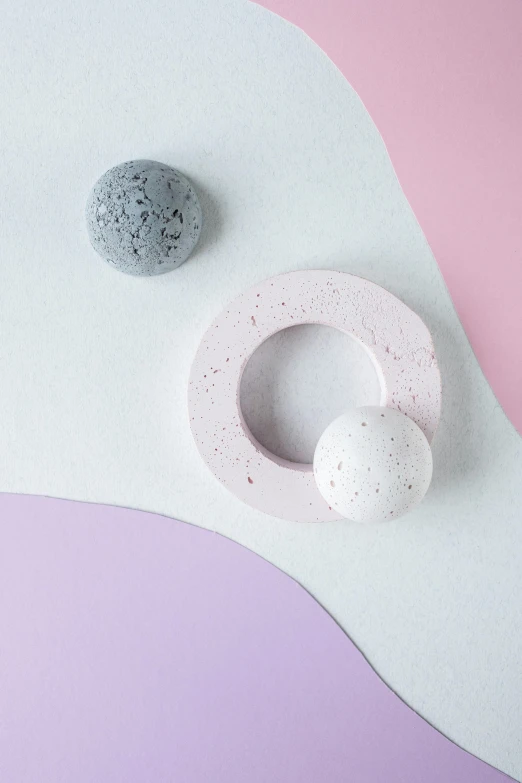 a white object sitting on top of a pink and purple surface, trending on unsplash, concrete art, rings, mini planets, grey, detailed product image