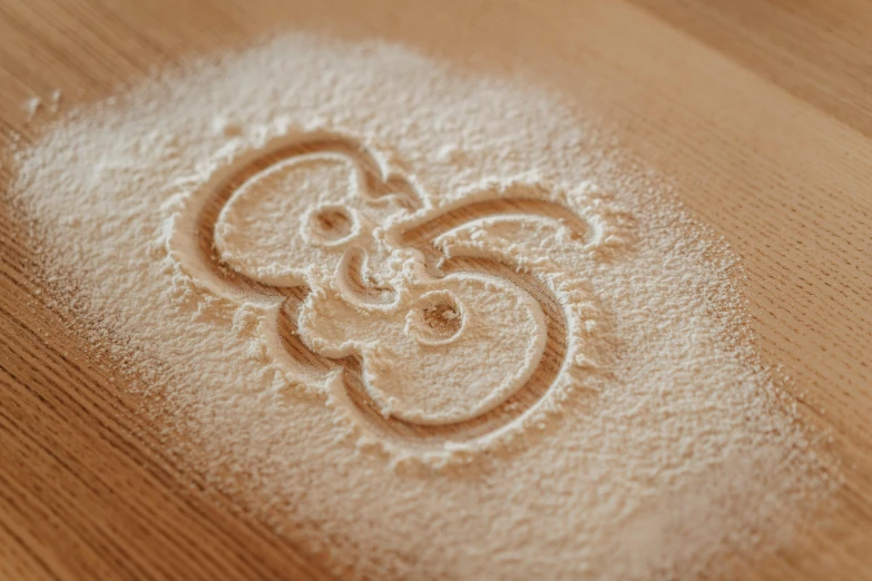 a wooden table topped with white powder on top of a wooden table, a stipple, by Adam Marczyński, trending on pexels, barn owl symbol in chest, covered in white flour, letter s, yinyang shaped