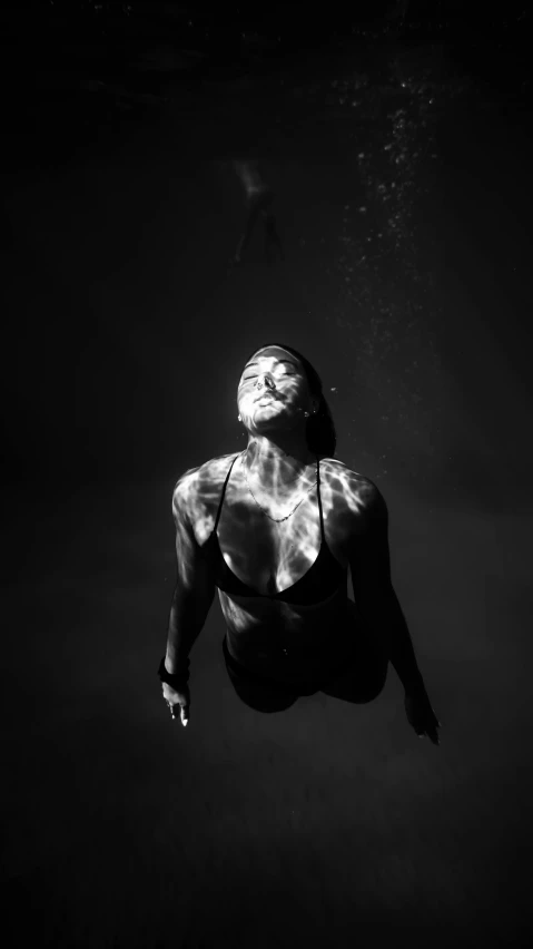 a black and white photo of a woman swimming, a black and white photo, glowing black aura, black female, sunburn, kneeling and looking up