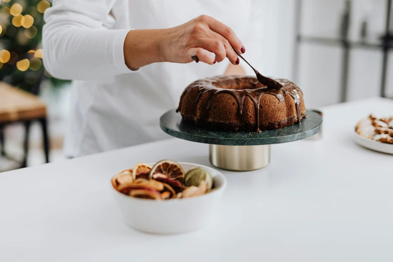 a woman is decorating a cake on a table, inspired by Richmond Barthé, trending on pexels, north island brown kiwi, chocolate sauce, arched back, for displaying recipes