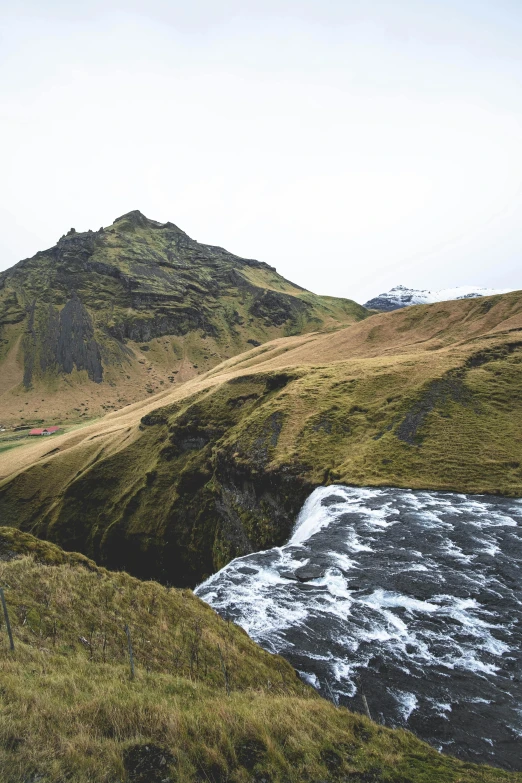 a man standing on top of a lush green hillside, by Hallsteinn Sigurðsson, trending on unsplash, hurufiyya, river flowing through a wall, “ aerial view of a mountain, small waterfall, winter