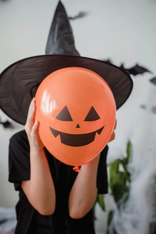 a child in a witch hat holding a balloon, face shown, orange, diy, zoom shot