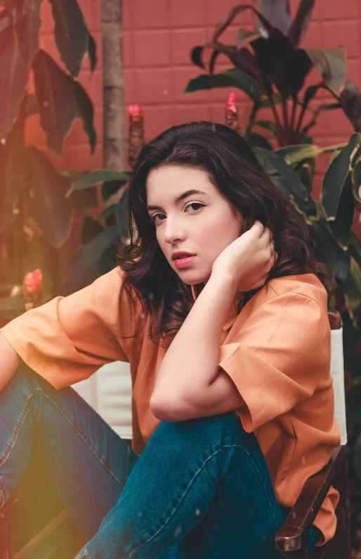 a woman sitting on a bench next to a potted plant, an album cover, pexels, portrait sophie mudd, wearing casual clothing, orange hue, dua lipa