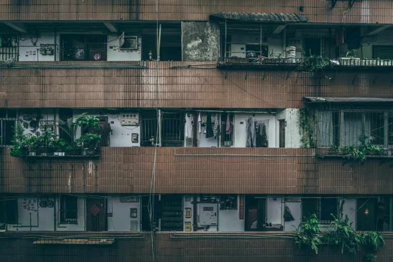 a tall building with lots of windows and plants on the balconies, a photo, inspired by Elsa Bleda, pexels contest winner, brutalism, slum, hong kong buildings, faded worn, ai weiwei and gregory crewdson