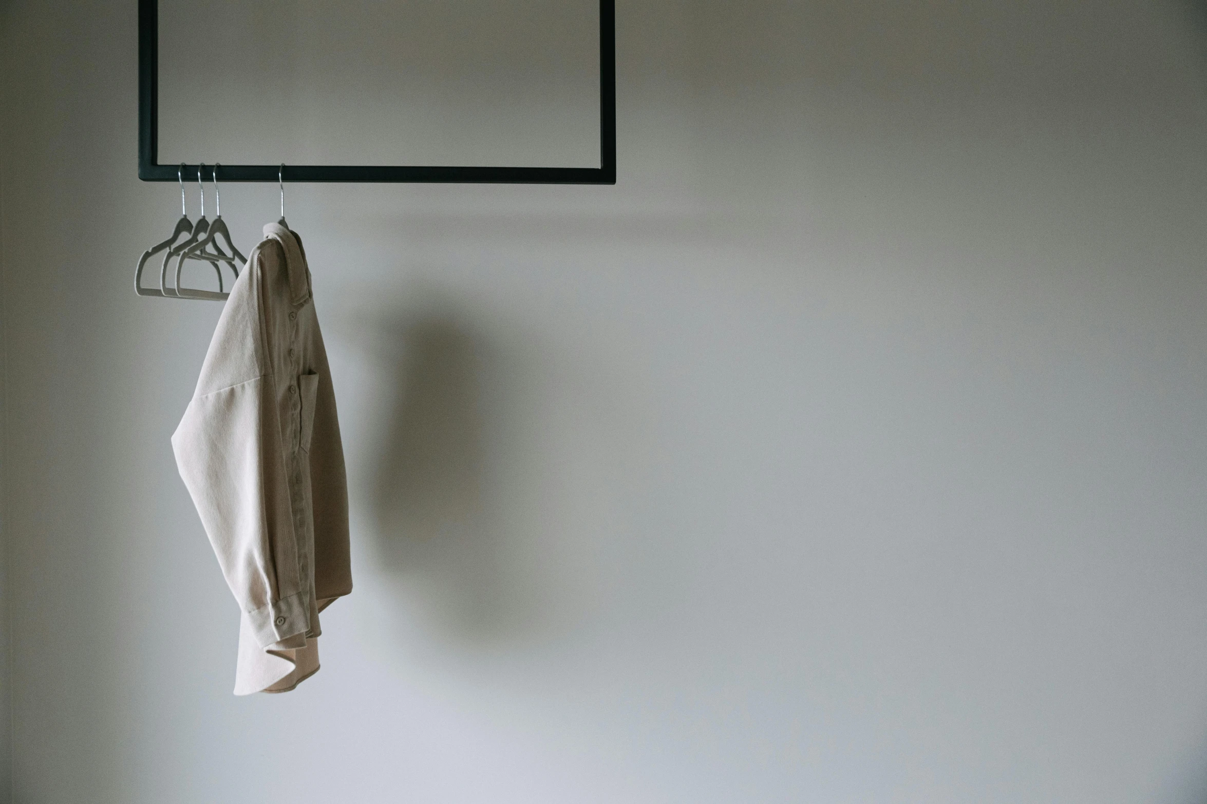 a white shirt hanging on a hanger on a wall, unsplash, light brown coat, sparse room, shot on sony a 7, wall ]