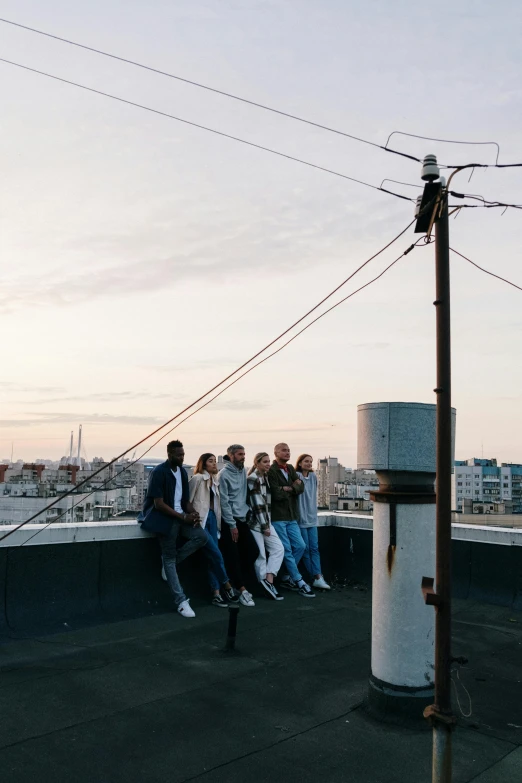 a group of people standing on top of a roof, by Jacob Toorenvliet, wires and lights, seaview, millennial vibes, low quality photo