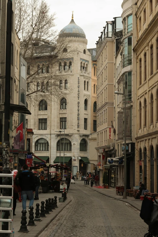 a group of people walking down a street next to tall buildings, art nouveau, istanbul, broadway, grey, shops