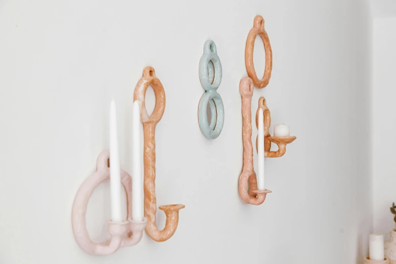 a couple of hooks mounted to the side of a wall, inspired by Louise Bourgeois, baroque, pastel glaze, holding a candle holder, looping, 3 - piece