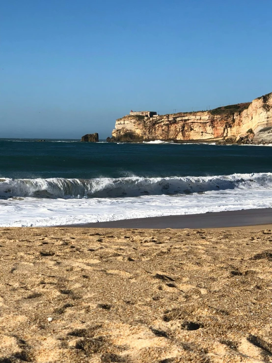 a surfboard sitting on top of a sandy beach, chalk cliffs above, bay area, victorian arcs of sand, byzantine