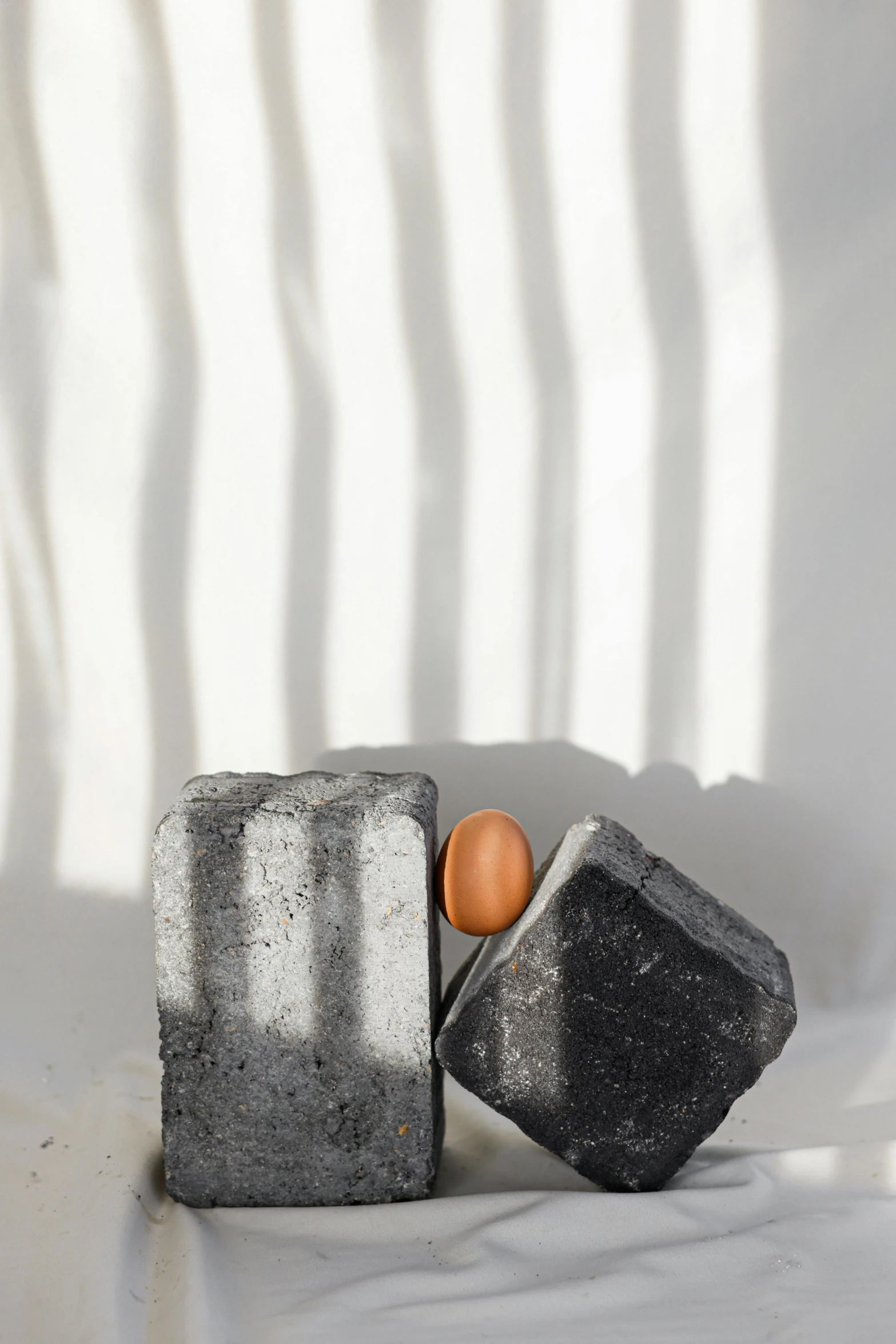 a couple of rocks sitting on top of a white surface, an abstract sculpture, by Sigrid Hjertén, unsplash, egg yolk, black and terracotta, sun overhead, charcoal color skin