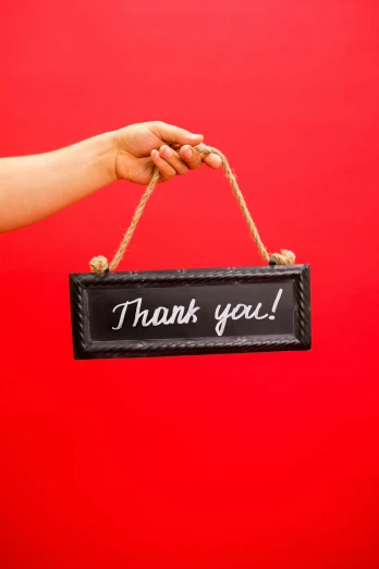 a person holding a sign that says thank you, by Rachel Reckitt, shutterstock contest winner, black steel with red trim, hanging rope, chalk, smol