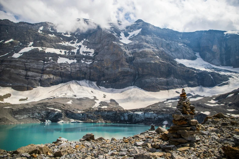 a man standing on top of a mountain next to a lake, by Brigette Barrager, pexels contest winner, hurufiyya, blue glacier, towering above a small person, canada, avatar image