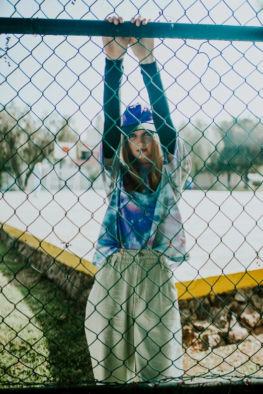 a woman holding a baseball bat over a fence, a picture, inspired by Elsa Bleda, trending on pexels, patterned clothing, teenager, netting, blue outfit