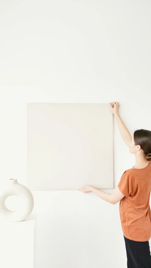a woman standing in front of a large white board, a minimalist painting, terracotta, thumbnail, square, beige