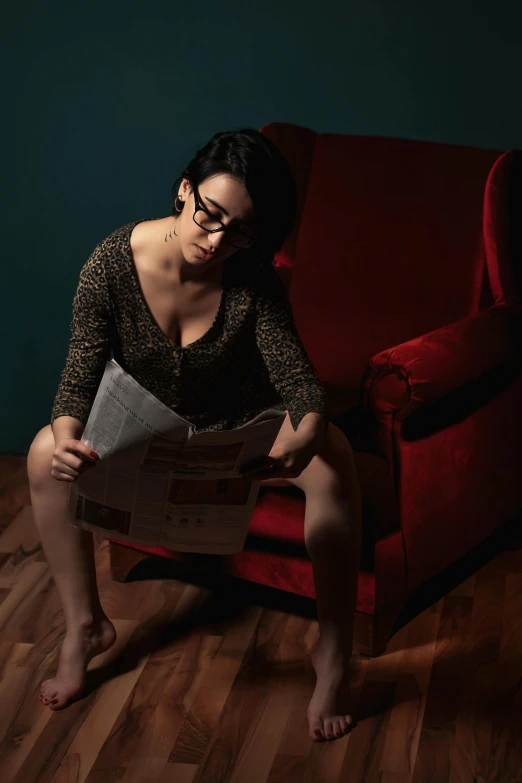 a woman sitting on a red couch reading a newspaper, an album cover, by Andrew Domachowski, pexels contest winner, serial art, reading glasses, shot at dark with studio lights, ana de la reguera portrait, seducing