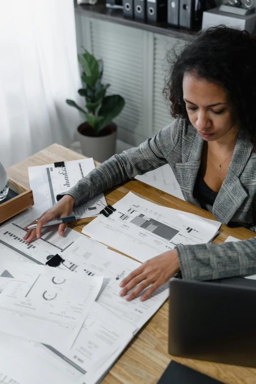 a woman sitting at a table with papers and a laptop, centered design, complex design, less detailing, on a desk