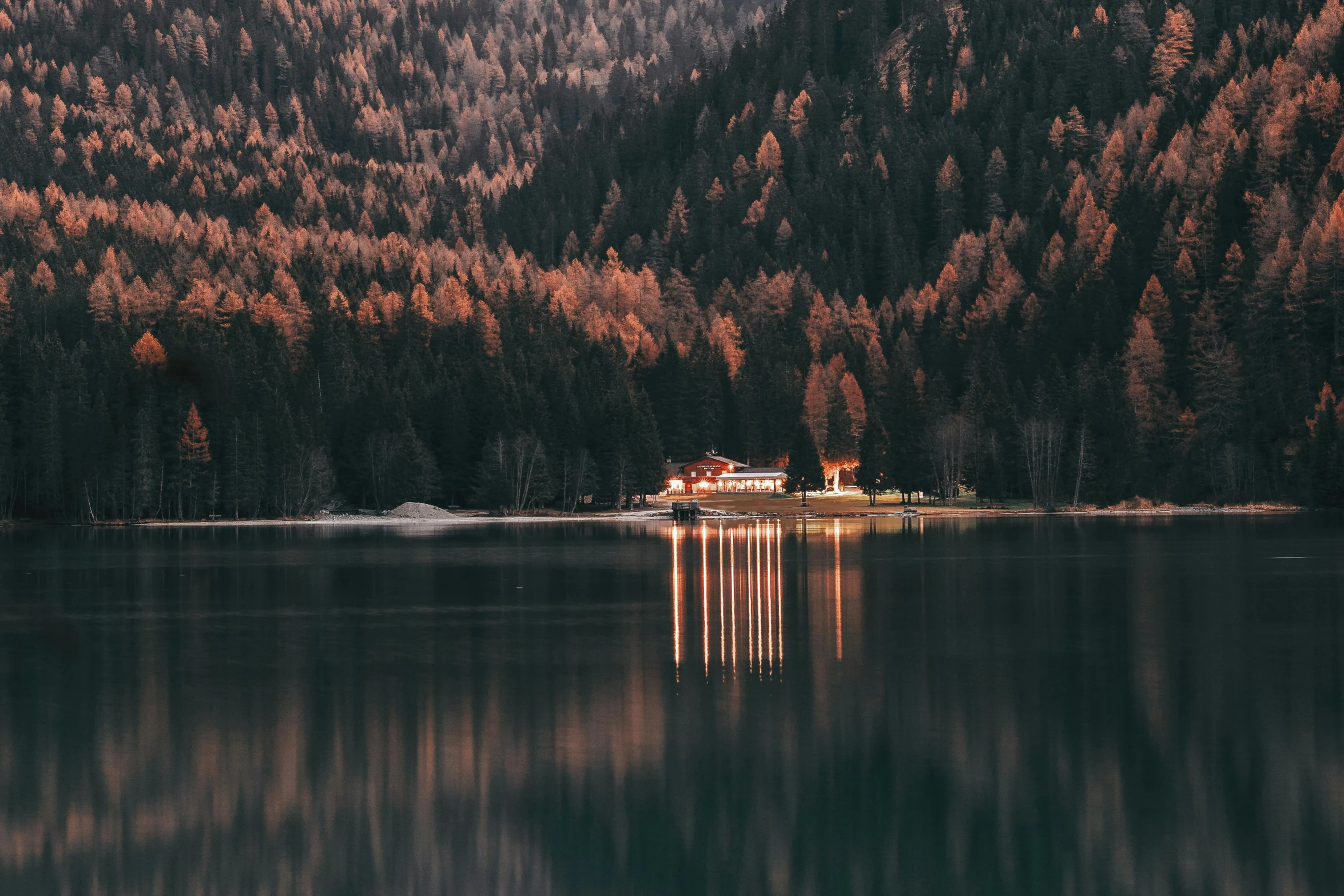 a house in the middle of a lake surrounded by trees, by Sebastian Spreng, pexels contest winner, cabin lights, in the dolomites, zoomed out to show entire image, pine trees in the background