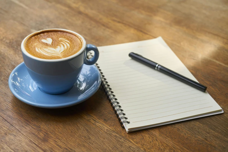 a cup of coffee and a notebook on a table, 9 9 designs, thumbnail, blue, no cropping