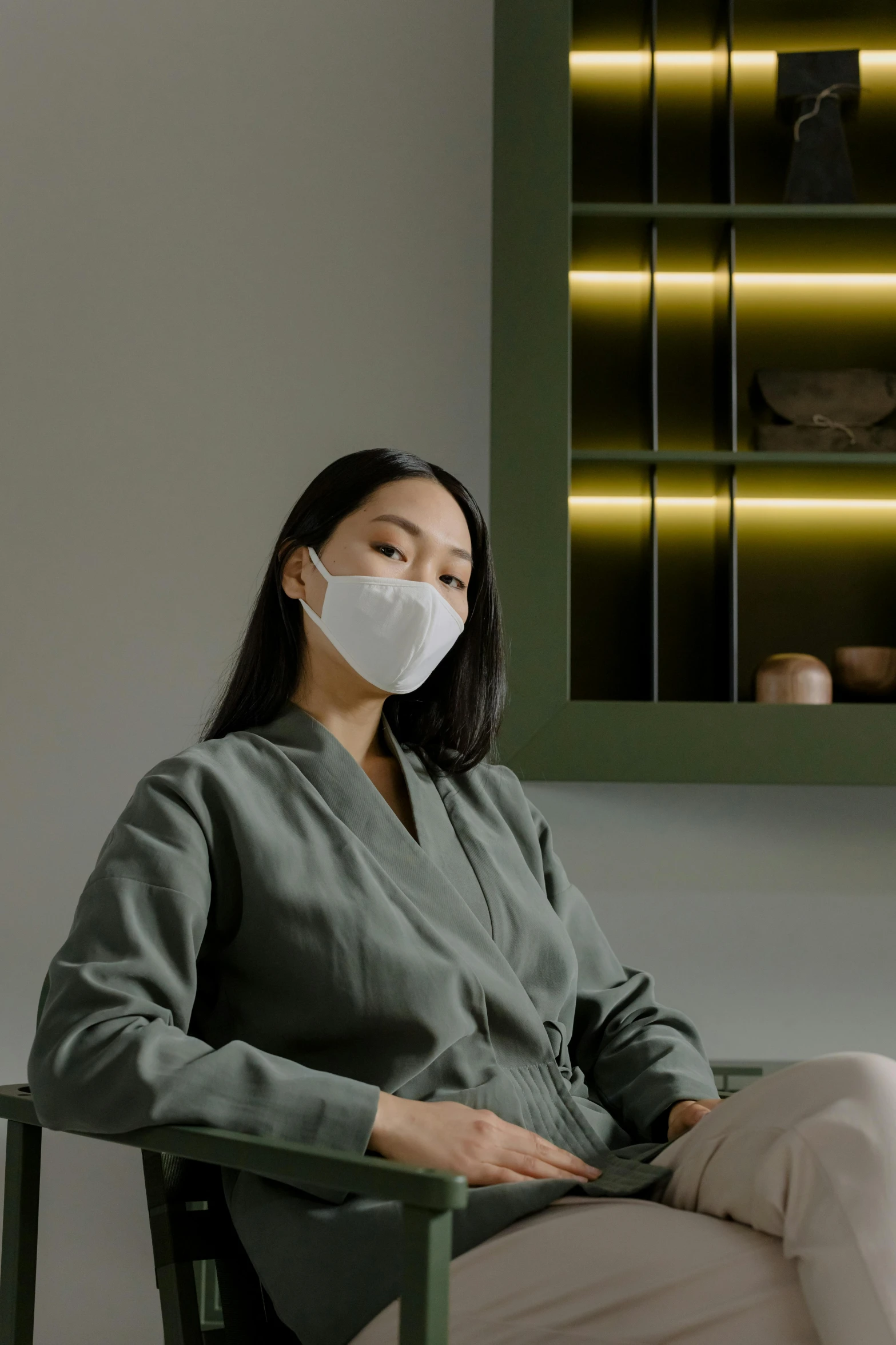 a woman sitting in a chair wearing a face mask, inspired by Kanō Naizen, trending on pexels, minimalism, wearing nanotech honeycomb robe, sitting on a store shelf, sitting in a waiting room, promotional image