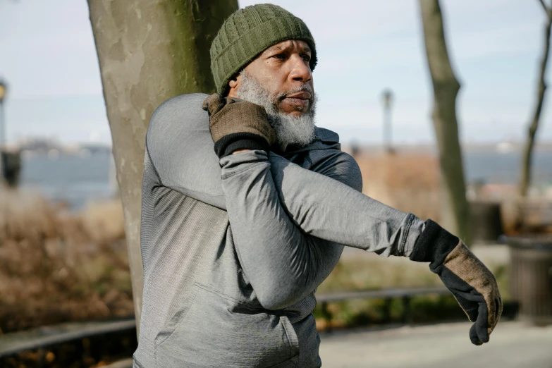 a man in a hat and gloves leaning against a tree, pexels contest winner, wearing fitness gear, old gigachad with grey beard, jamel shabazz, handling riffle on chest
