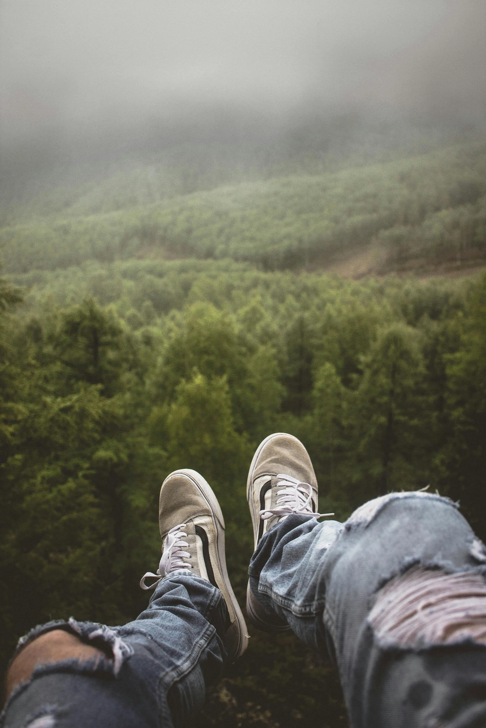 a person sitting on top of a lush green hillside, a picture, by Jacob Toorenvliet, trending on pexels, realism, detailed shot legs-up, over the tree tops, on a rainy day, sneaker photo