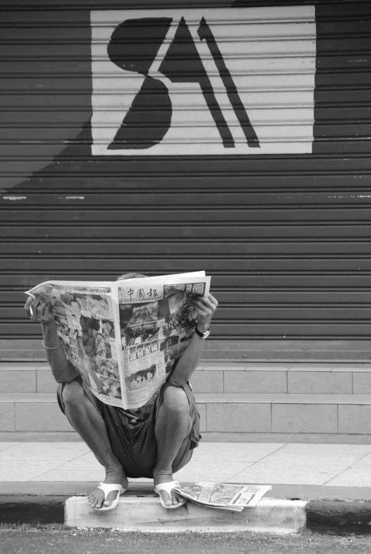 a man sitting on a curb reading a newspaper, a black and white photo, by Joze Ciuha, pexels contest winner, street art, gif, comic book, deep!!!!!, in front of a garage