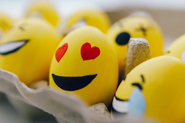 a carton of eggs with smiley faces painted on them, a cartoon, trending on pexels, yellow, smiling spartan, heart-shaped face, blurred