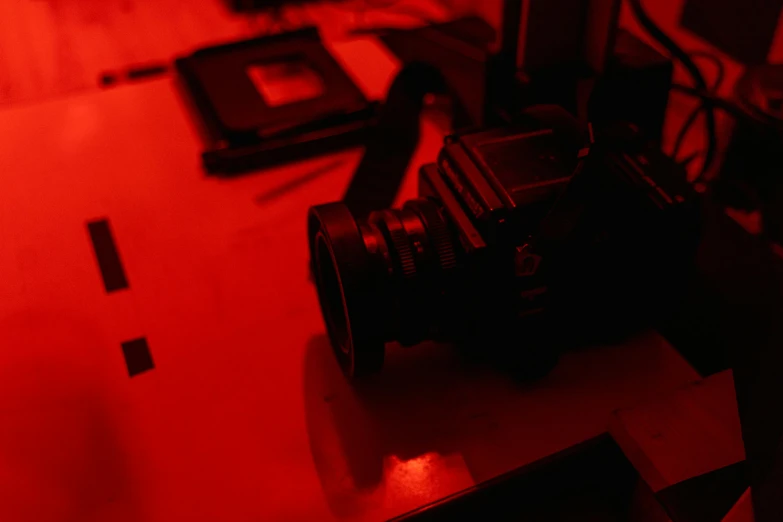 a camera sitting on top of a table under a red light, a picture, darkroom, horror footage, medium format, film footage