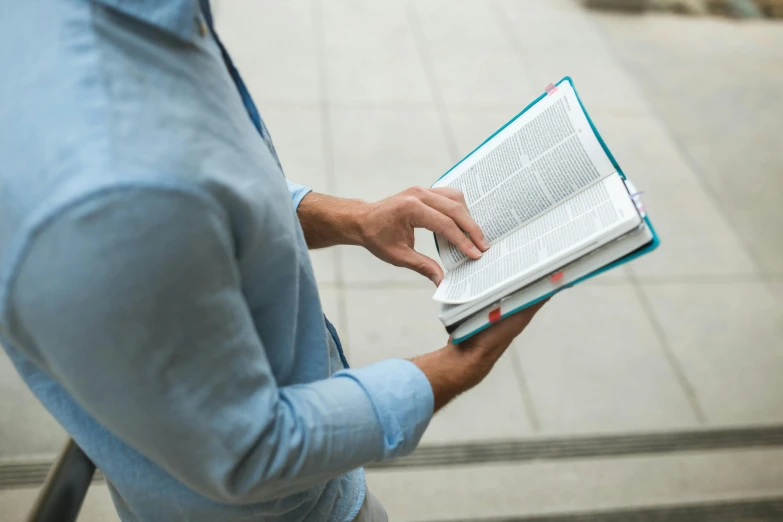 a man in a blue shirt is reading a book, by Carey Morris, unsplash, unilalianism, he is holding a large book, then leave it to god, student, pastel'