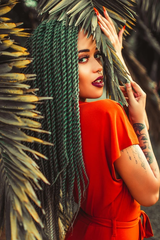 a woman with green dreadlocks standing in front of a palm tree, inspired by Elsa Bleda, trending on pexels, renaissance, rich red colors, with tattoos, portrait of vanessa morgan, dark green hair