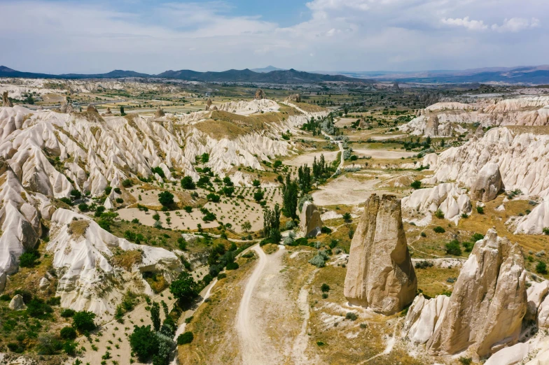 a dirt road in the middle of a valley, by Muggur, pexels contest winner, art nouveau, white rocks made of bone, cypresses, wide aerial shot, 2000s photo