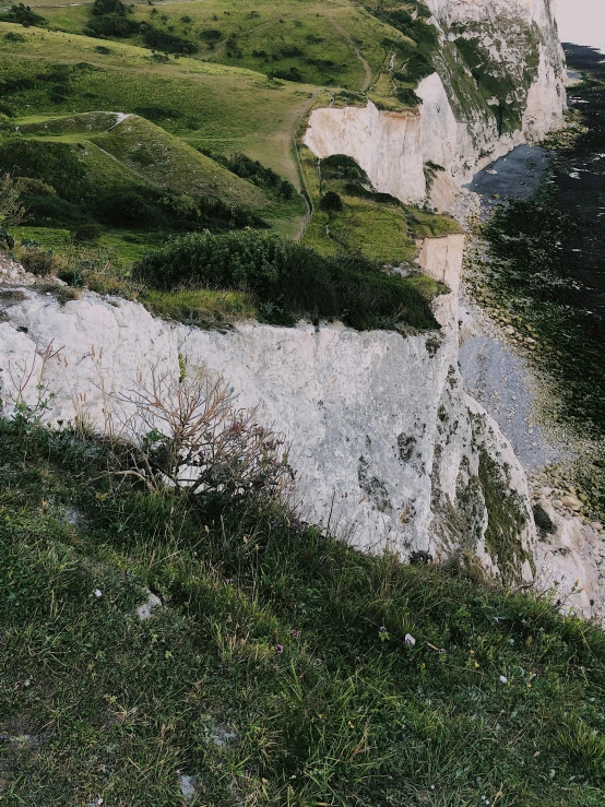 a red fire hydrant sitting on top of a lush green hillside, an album cover, by Muggur, unsplash, les nabis, cliffs of dover, gigapixel photo, white rocks made of bone, very poor quality of photography