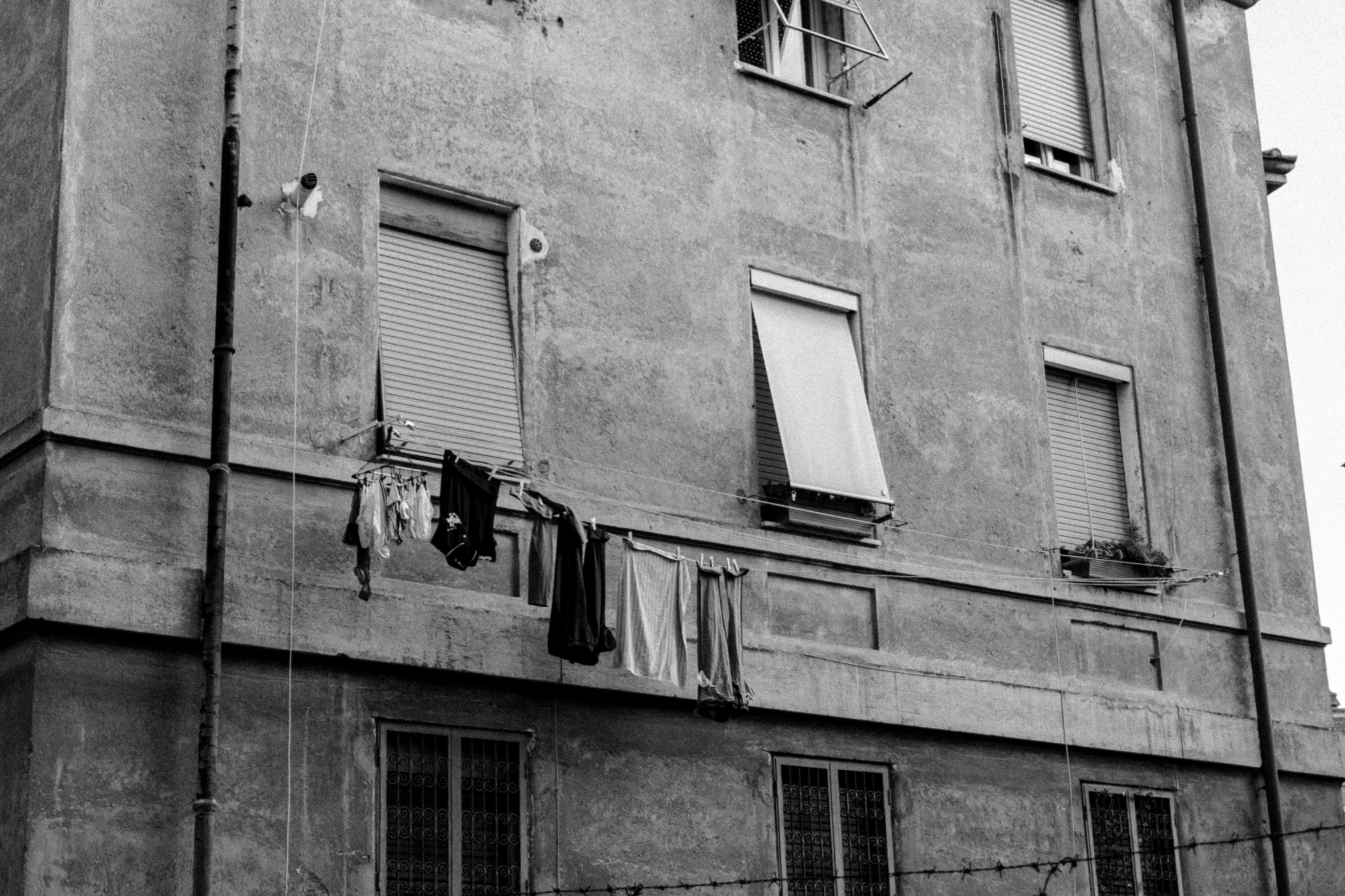 a black and white photo of a building with clothes hanging out to dry, by Alessandro Allori, a messy, shutters, dressed in a worn, spying