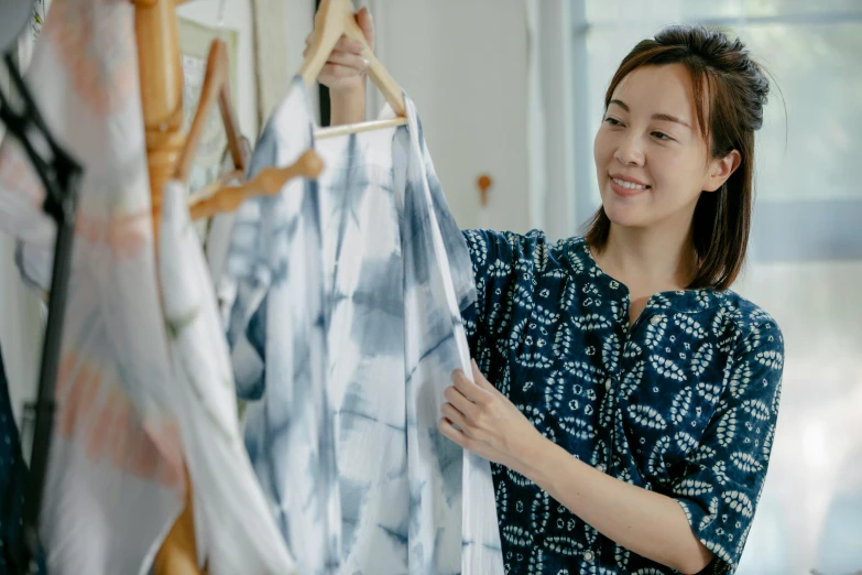 a woman standing in front of a rack of clothes, a silk screen, inspired by Miyagawa Chōshun, pexels contest winner, wearing a linen shirt, avatar image, candid shot, asian woman made from origami