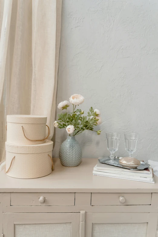 a table with a stack of boxes on top of it, a still life, inspired by Emil Carlsen, shutterstock contest winner, romanticism, beige color scheme, elegant flowers, serene bedroom setting, glassware