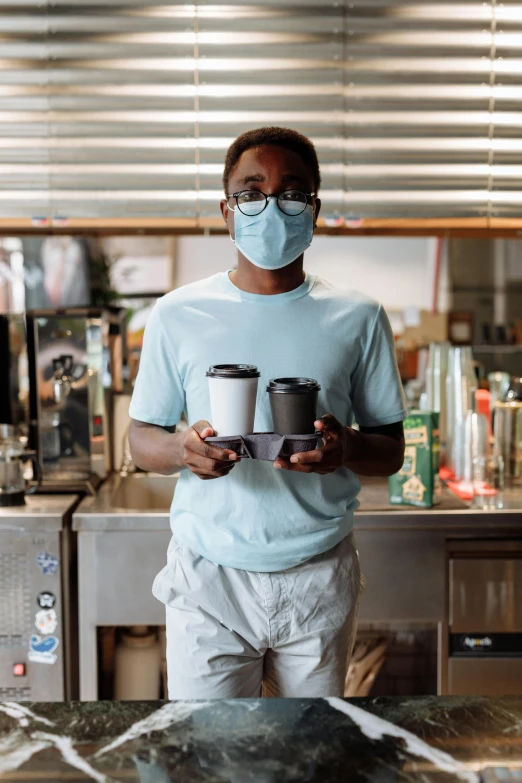 a man wearing a face mask holding two cups of coffee, by Austin English, market, thumbnail, standing, dark skinned